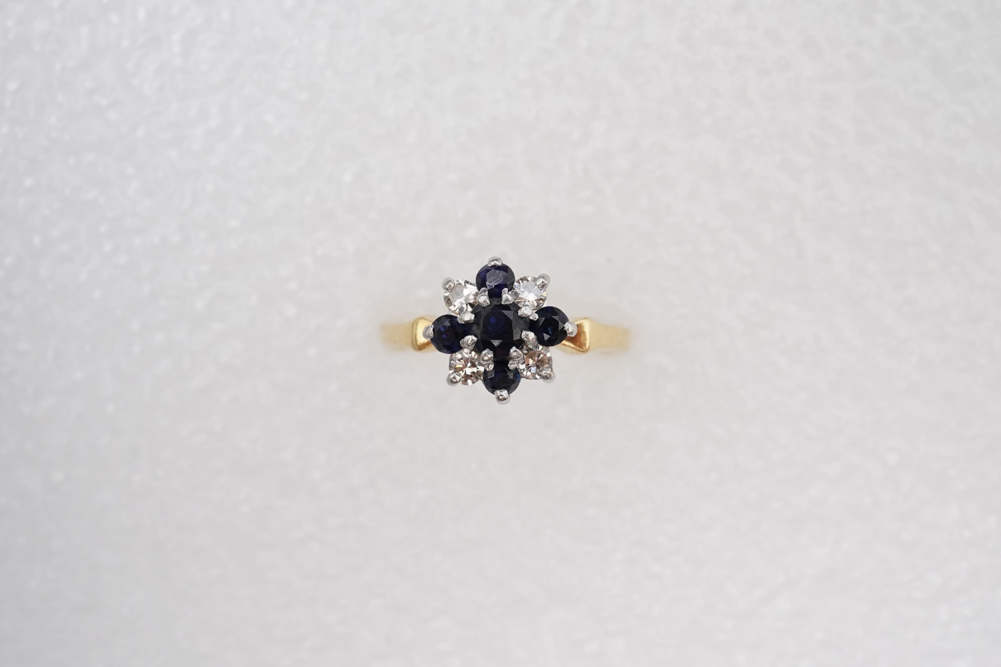 A sapphire and diamond cluster ring, set with circular-cut sapphires and brilliant-cut diamonds totalling approximately 0.20 carats, mounted in gold and platinum, size M, stamped 18CT PLAT, gross weight approximately 3.5